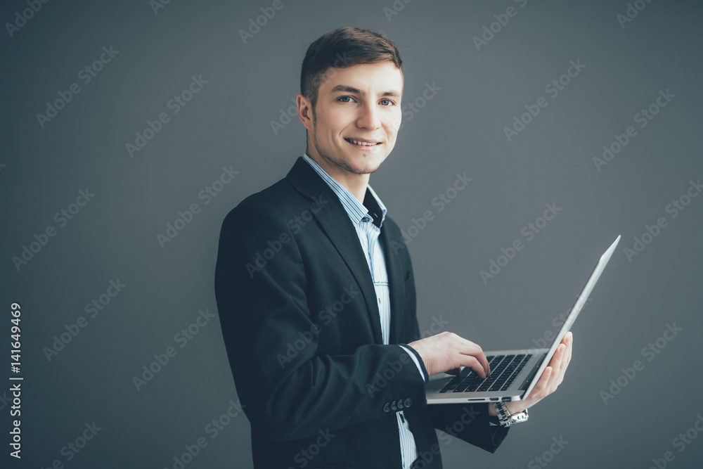 Handsome young businessman is using a laptop, looking at camera and smiling, on black background Handsome young businessman is using a laptop, looking at camera and smiling, on black background