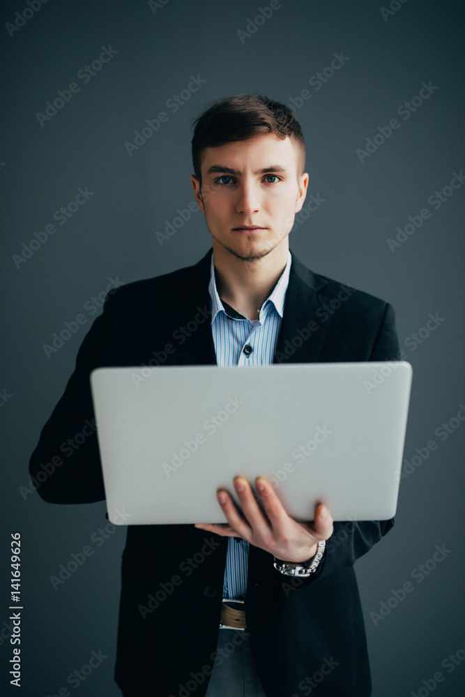 Handsome young businessman is using a laptop, looking at camera and smiling, on black background Handsome young businessman is using a laptop, looking at camera and smiling, on black background