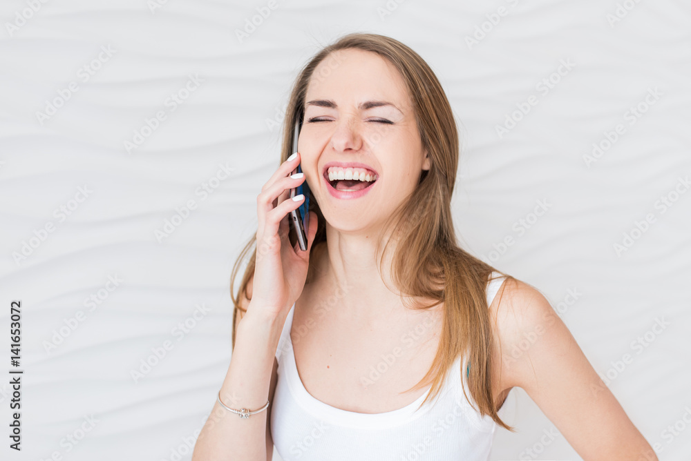 Young laughing girl in white singlet speaking over phone on a white background Young laughing girl in white singlet speaking over phone on a white background