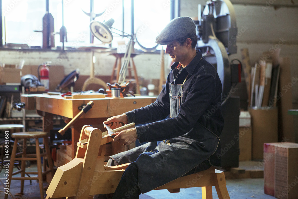 Side view of carpenter shaving wood with drawknife in workshop Side view of carpenter shaving wood with drawknife in workshop