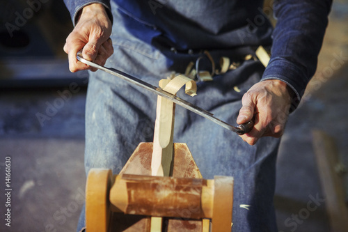 Midsection of carpenter shaving wood with drawknife at workshop photo