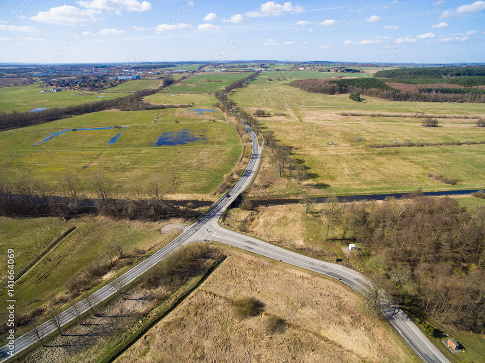 Aerial view of a country road with crossing between agriculture fields and blue sky