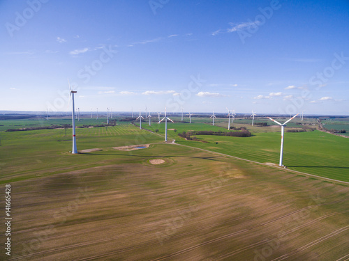 aerial view panorama of green agriculture fields with blue sky and wind turbines in the background