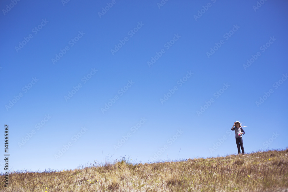 Girl looking through binoculars while standing on grassy field against clear blue sky Girl looking through binoculars while standing on grassy field against clear blue sky