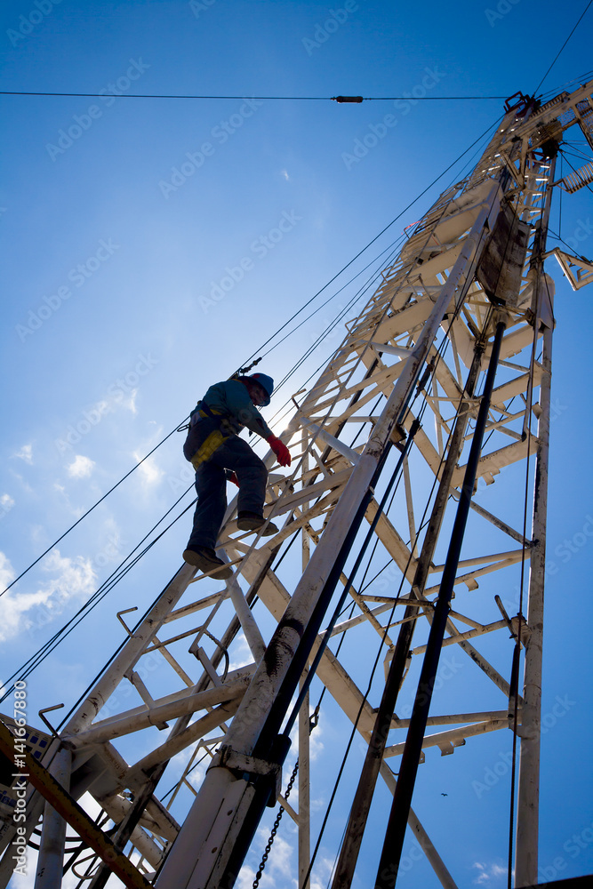 Low angle view of worker climbing on crane against blue sky Low angle view of worker climbing on crane against blue sky