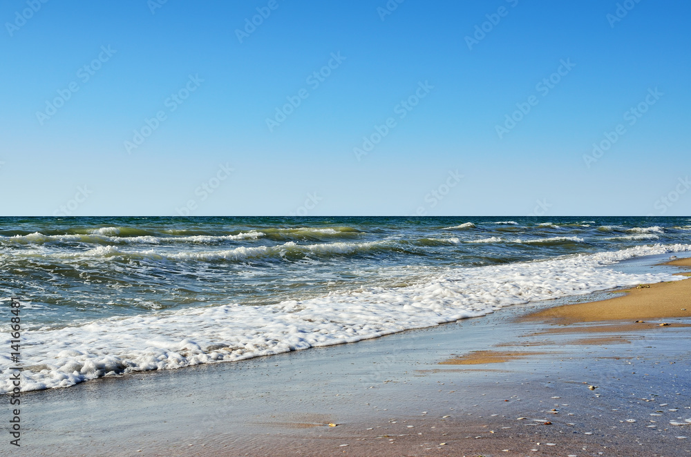 Sea waves wash the beach against a blue sky