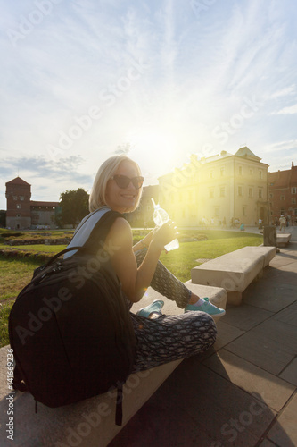 Female traveler sitting and enjoys the view of Wawel Castle with a bottle of water in the rays of sunlight. Krakow, Poland