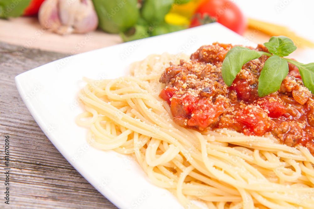Spaghetti bolognese,some tomatoes, olive oil, basil, garlic, and raw pasta in the background Spaghetti bolognese,some tomatoes, olive oil, basil, garlic, and raw pasta in the background