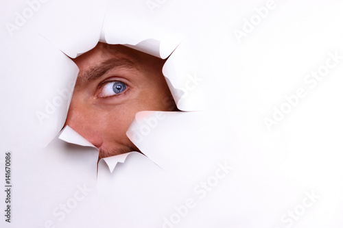 A curious eye looks into the torn hole on a white sheet