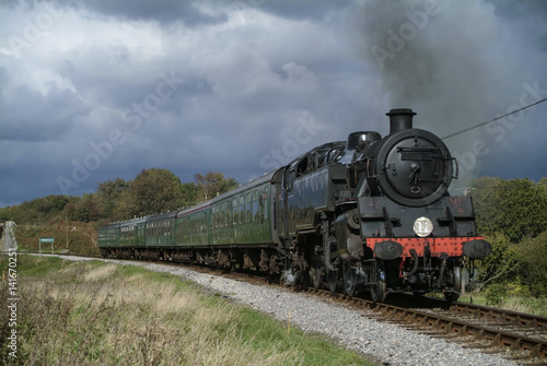 Black steam locomotive with green carriages approaching on track from left to right