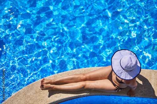The girl with a hat sits on the edge of the pool. Top view.
