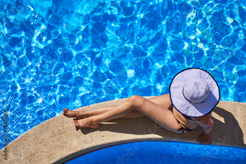The girl with a hat sits on the edge of the pool. Top view.