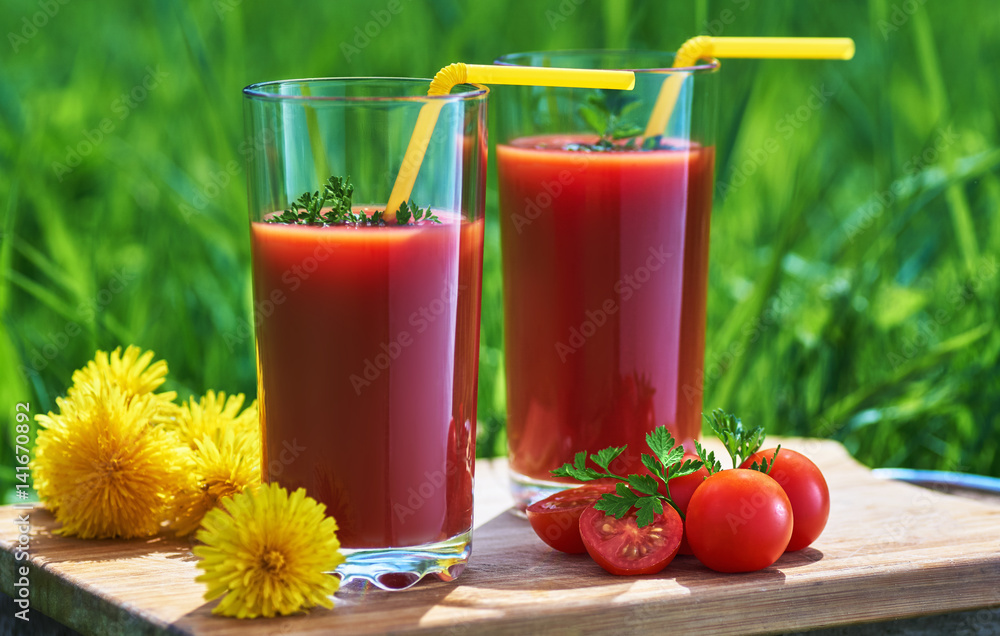 Glass with tomato juice on a tray near dandelions Glass with tomato juice on a tray near dandelions
