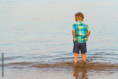 Wall Mural Little boy walks barefoot in shallow sea water