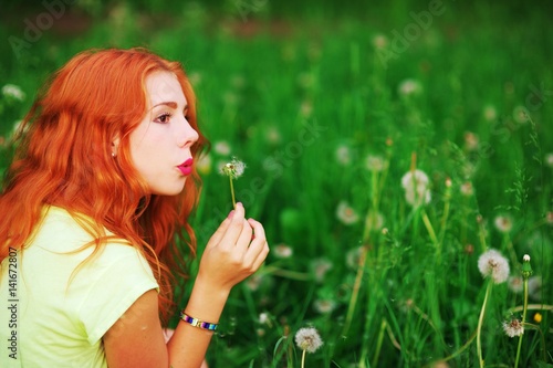 beautiful red-haired young woman blowing away dandelion outdoors