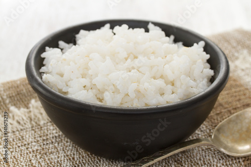 boiled rice in black bowl in wooden background