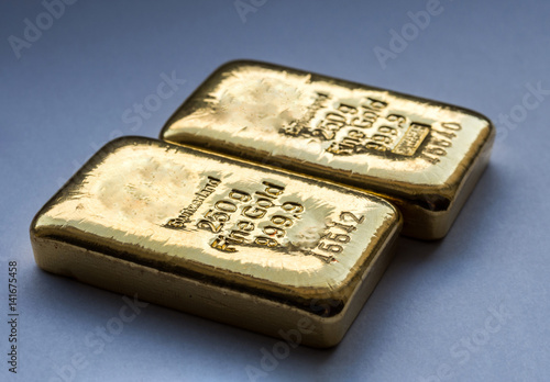 Two cast gold bars weighing 250 grams on a blue background. Selective focus.