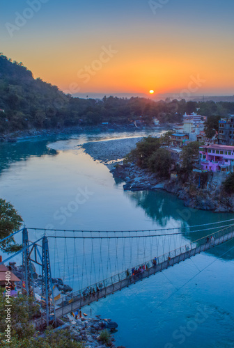 View of River Ganga and Lakshman Jhula bridge at sunset with a blue sky and colorful houses. Rishikesh. India. HDR image photo