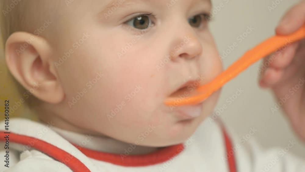 Mom feeds a small child with a spoon of vegetable puree, close-up Mom feeds a small child with a spoon of vegetable puree, close-up