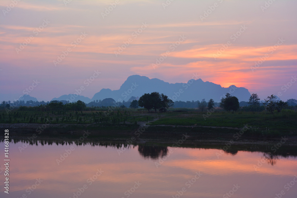 Colorful tropical sunset. Rice feilds and mountains reflecting in the water.