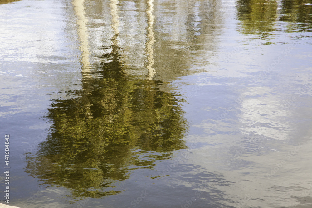 Trees and clouds being reflected in water with small waves Trees and clouds being reflected in water with small waves