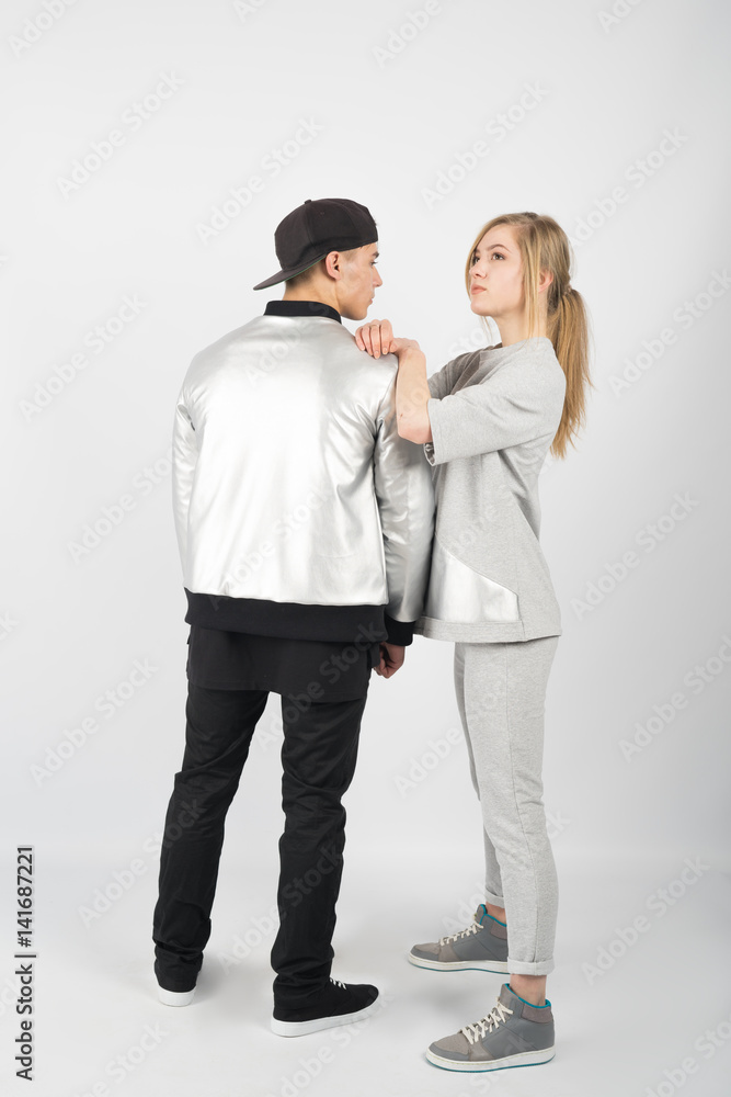 Boy and girl. Young muscular man wearing black clothes ,grey jacket and snapback with girl in grey casual suit on white background Boy and girl. Young muscular man wearing black clothes ,grey jacket and snapback with girl in grey casual suit on white background