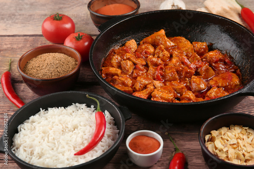 Frying pan with delicious chicken tikka masala and bowl with rice on wooden table