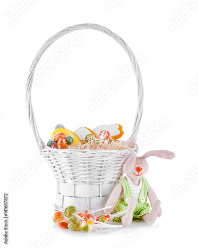 Delicious Easter gifts in basket with decorative rabbit on white background