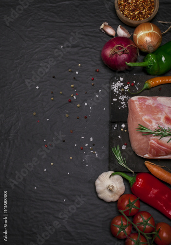 Raw pork meat on a cutting board with rosemary, vegetables and spices.