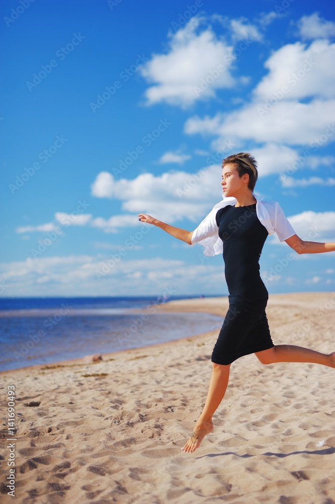 Wonderful portrait of a young slim woman in a black dress with a white Bolero, running barefoot on the sand to sea on background of blue sky and white clouds of air. Wonderful portrait of a young slim woman in a black dress with a white Bolero, running barefoot on the sand to sea on background of blue sky and white clouds of air.