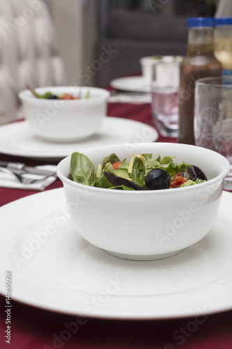 Green Salad with Lettuce, Tomato, Avocado and Olives served in White Dinnerware and Red Table Cloth