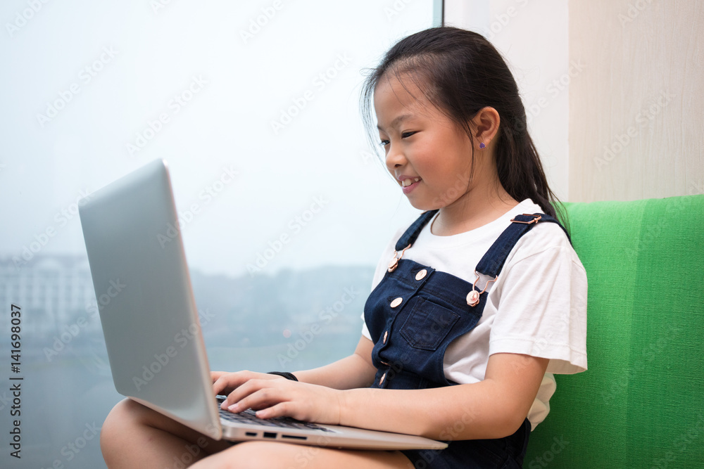 Asian Chinese little girl using laptop on the windowsill