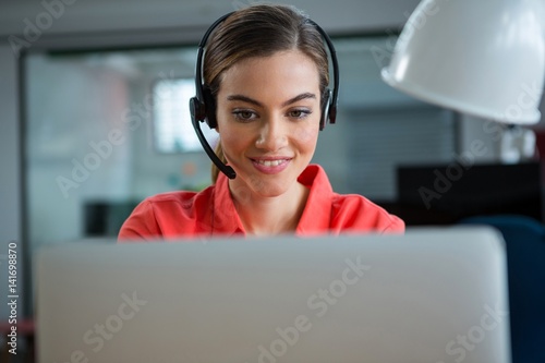  Smiling female executive working on her laptop while calling