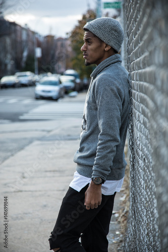 Obraz na plátně A young, hip man poses for a pensive portrait along a fence in NYC