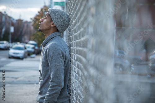 A young, hip man poses for a pensive portrait along a fence in NYC