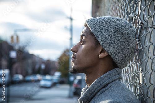 A young, hip man poses for a pensive portrait along a fence in NYC