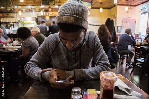 A young man looks at his phone while waiting for his meal