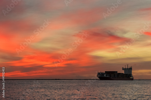 Red container ship arriving from Baltic sea at red sunset sky