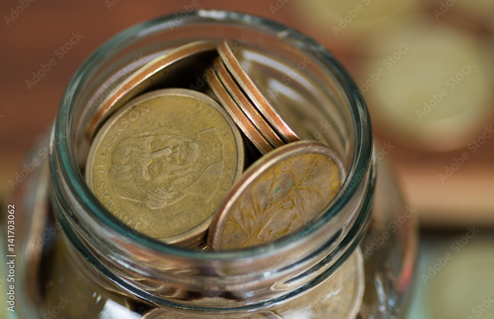 Close up glass jar opening filled up with dollar coins Close up glass jar opening filled up with dollar coins
