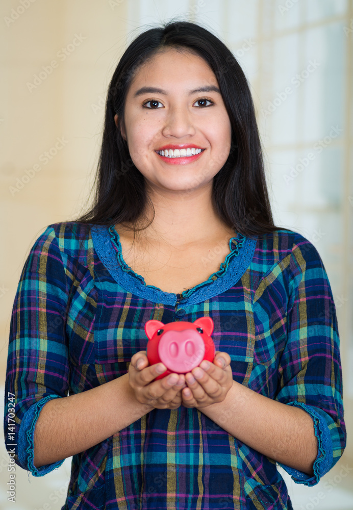 Young brunette woman facing camera, holding piggy bank and smiling happily Young brunette woman facing camera, holding piggy bank and smiling happily