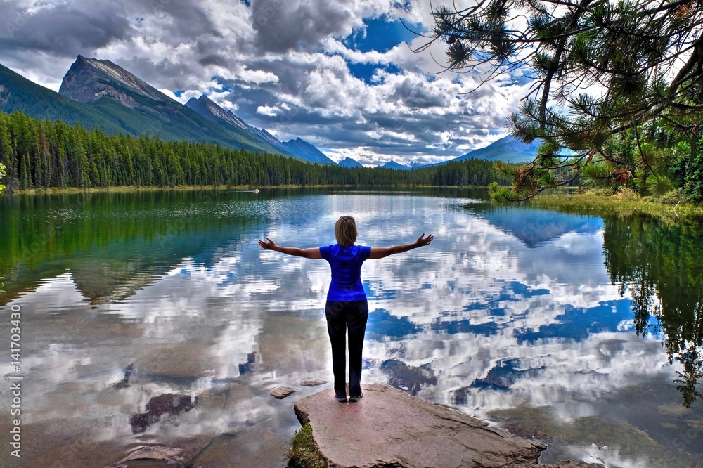 Young woman embracing the lake with reflections of clouds and mountains. Honeymoon lake.  Banff National Park. Canadian Rockies. Alberta. Canada.