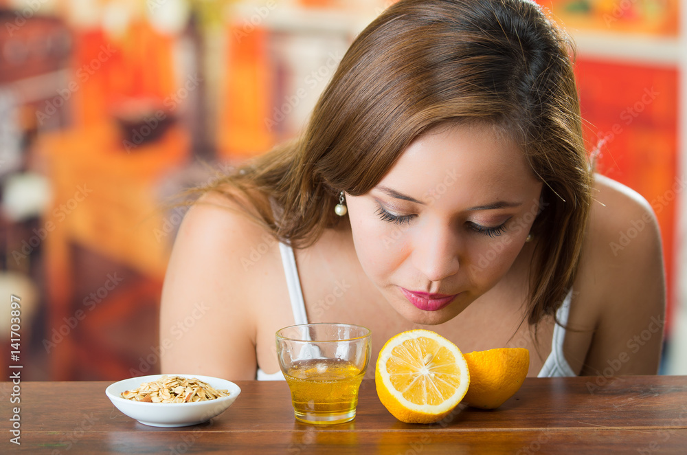 Young brunette bending over table smelling sliced lemon, glass of honey and some granola on the side Young brunette bending over table smelling sliced lemon, glass of honey and some granola on the side