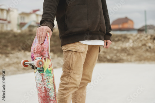 Close up Teenager standing in a right side hoodie holding a hand skateboard on the background slum photo