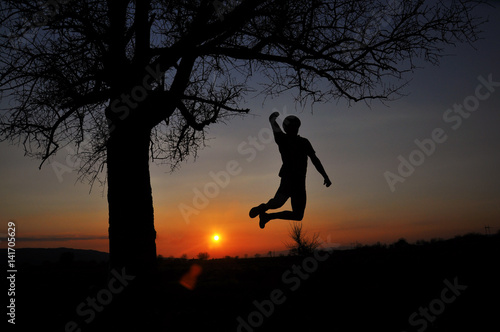 Silhouette of  man jumping in the air under a big tree. Happy man got a great idea and celebrate