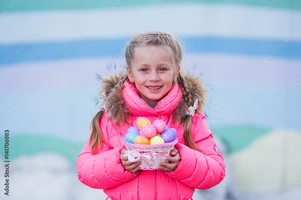 Nice cute little girl with two pigtails goes on a visit to the celebration of Easter with a basket of colorful eggs Nice cute little girl with two pigtails goes on a visit to the celebration of Easter with a basket of colorful eggs