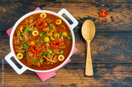 Slow Cooker Ropa Vieja, Cuban famously delicious shredded beef stew with pepper and olives in a white casserole on the wooden table. Top view. photo