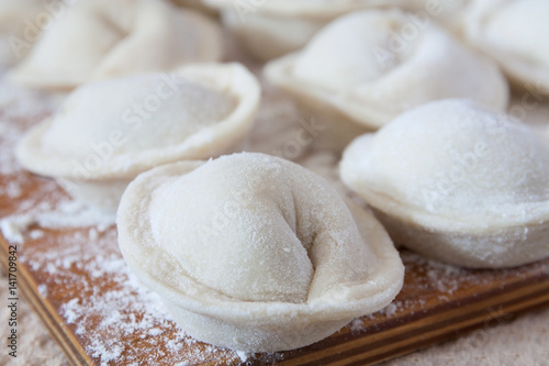 Process of making homemade pelmeni (dumplings) on wooden board - traditional dish of Russian cuisine. Selective focus