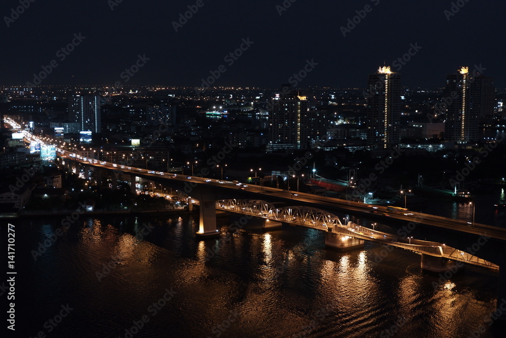 night picture of car crossing bridge in Bangkok over Chao Phraya River with slow shutter speed 