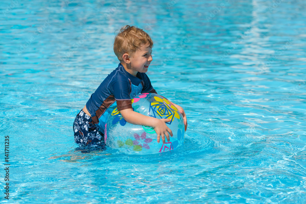 Little boy in a swimming suit plays with an inflatable transparent