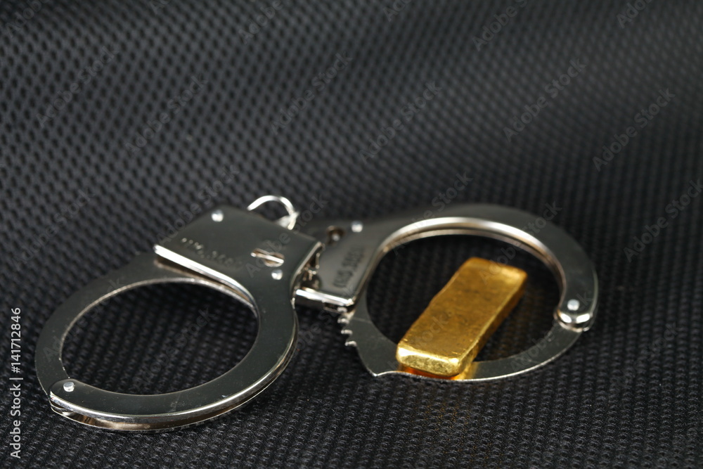 The chrome metal handcuffed and gold bar represent the crime fraud and punishment equipment concept related idea. The chrome metal handcuffed and gold bar represent the crime fraud and punishment equipment concept related idea.